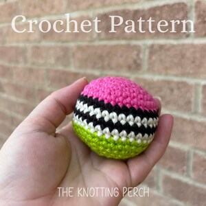 May include: A spherical crochet object featuring horizontal stripes in bright pink, black, white, and lime green. The text "Crochet Pattern" appears at the top and "THE KNOTTING PERCH" is printed at the bottom of the image.