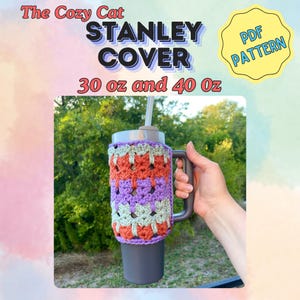 May include: A crochet cover for a 30 oz or 40 oz Stanley tumbler. The cover is made in a multi-colored striped pattern with orange, purple, and green yarn. The cover is shown on a gray tumbler with a black handle.