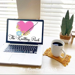 Pu&ograve; includere: Un computer portatile con uno sfondo bianco e il testo "The Knotting Perch" sullo schermo. Il computer portatile &egrave; su un tavolo di legno con una tazza di caff&egrave; e un sottobicchiere all'uncinetto con frange.