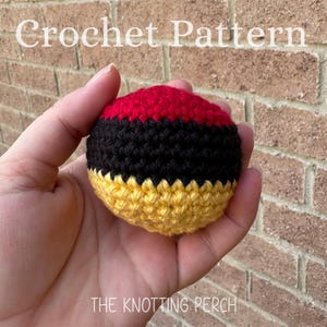 May include: A spherical crochet item featuring horizontal bands of red, black, and yellow yarn. The text "Crochet Pattern" is visible at the top, and "THE KNOTTING PERCH" is printed at the bottom of the image against a brick background.