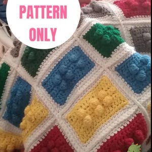 May include: A crochet blanket featuring a grid of rectangular blocks in red, blue, yellow, green, and grey, each with raised circular textures. The blanket has white borders between the blocks. Text on the image reads: DIGITAL PATTERN ONLY.