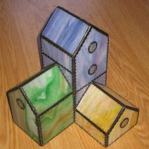 Peut inclure: Trois maisons en verre teinté, une violette, une verte et une jaune, sont disposées en forme de triangle. Les maisons ont des bordures noires et des fenêtres rondes.