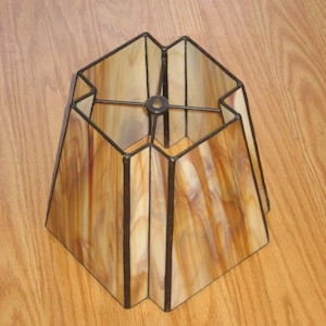 Puede incluir: Una pantalla de lámpara de vidrio tintado de forma cuadrada con un patrón de mármol marrón y blanco. La pantalla tiene un marco de metal negro.