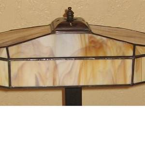 May include: A stained glass lamp with a brown base and a beige and brown glass shade. The shade has a geometric design and a finial on top.