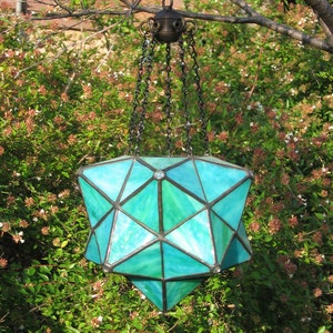 May include: A turquoise stained glass pendant light fixture hangs from a chain. The light fixture is shaped like a star and has a geometric design.