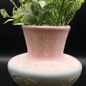 May include: A pink and blue ceramic vase with a geometric design. The vase has a wide base and a narrow neck. It is decorated with white lines and patterns.