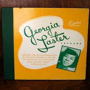 May include: A yellow and green record album cover with the text "Georgia Paster Soprano" and a photo of a woman with a microphone. The album is titled "Cathedral Records".