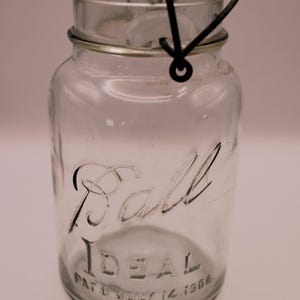 May include: A clear glass Ball Ideal jar with a wire bail closure. The jar has the text "Ball Ideal" and "Pat'd June 14, 1906" etched into the glass.