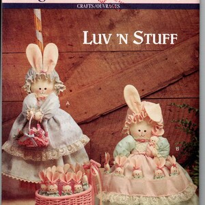 May include: Butterick 6029 sewing pattern envelope featuring Luv 'N Stuff. The image displays two fabric rabbit dolls wearing bonnets and dresses with lace trim. One doll holds a pink basket filled with small rabbits, and the other holds a small doll.