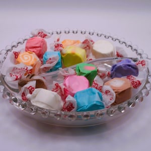 May include: A clear glass bowl filled with colorful candies. The candies are wrapped in red and white paper and are arranged in a decorative pattern.