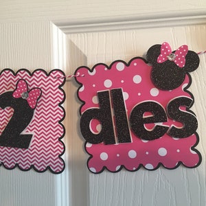 May include: A pink and black banner with a white chevron pattern and white polka dots. The banner says "2 dlles" with a black Minnie Mouse head in the middle.
