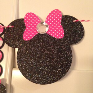 May include: Black and white glitter Minnie Mouse head with a pink and white polka dot bow and a clear rhinestone in the centre.