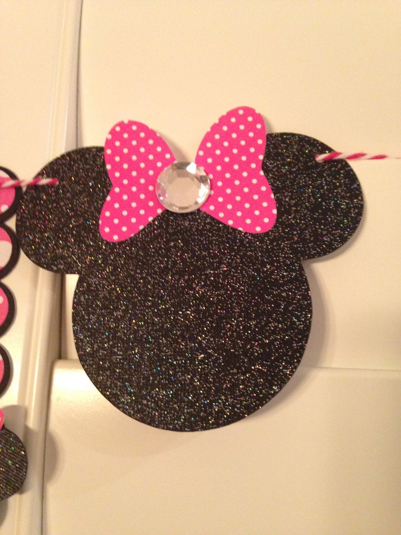 May include: Black and white glitter Minnie Mouse head with a pink and white polka dot bow and a clear rhinestone in the centre.