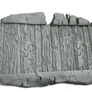Puede incluir: Un panel rectangular gris texturizado con un patrón de vetas de madera. El panel tiene un borde superior áspero e irregular y un borde inferior agrietado, lo que le da una apariencia desgastada. La veta de la madera presenta nudos y líneas verticales detalladas.