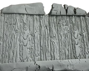 May include: A gray, textured, rectangular panel with a wood grain pattern. The panel has a rough, uneven top edge and a cracked bottom edge, giving it a weathered appearance. The wood grain features detailed knots and vertical lines.