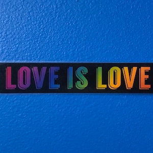 May include: A black rectangular sticker with the text "LOVE IS LOVE" in rainbow colors.