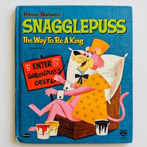 Peut inclure: Livre pour enfants vintage intitulé "Snagglepuss: The Way To Be A King" de Hanna-Barbera. La couverture présente un lion rose de dessin animé en tenue jaune, assis sur une chaise en bois. Le livre a un fond bleu avec le texte "Enter Snagglepuss's Castle".