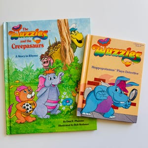 Könnte beinhalten: Zwei Kinderbücher mit farbenfrohen Illustrationen und dem Titel "Wuzzles". Ein Buch trägt den Titel "The Wuzzles and the Creepasaurs: A Story in Rhyme". Das andere Buch trägt den Titel "Hoppopotamus Plays Detective."