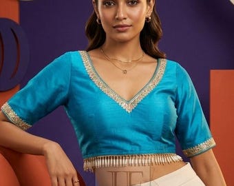 Peut inclure: Un chemisier court bleu turquoise avec un décolleté en V profond, des manches courtes et une broderie dorée sur les bords. L'ourlet présente une bordure à franges pendantes. Le chemisier est associé à un pantalon crème taille haute.
