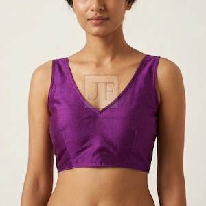 May include: A sleeveless, deep purple blouse featuring a V-neckline and a subtle, textured fabric finish. The garment has a fitted silhouette with visible vertical seam detailing on the front bodice and a watermark logo reading JF in the center.