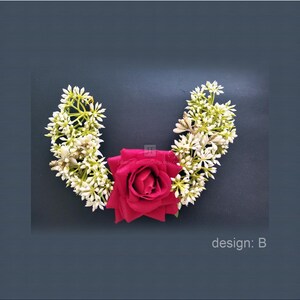 May include: A floral hair accessory featuring a deep red rose at the center, flanked by white and green floral arrangements. The design is set against a dark background, with the text "design: B" visible.