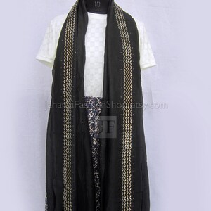 May include: A black scarf featuring two vertical gold zigzag embroidered stripes with small embedded studs. The scarf is draped over a white short-sleeved top with a subtle grid pattern and a blue and white floral print skirt on a mannequin.