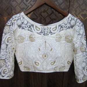 Könnte beinhalten: Weiße bestickte Bluse mit langen Ärmeln und einem runden Ausschnitt. Die Bluse ist aus einem durchsichtigen Stoff mit zarten Blumen- und Paisleymustern.