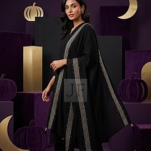 May include: A black tunic and matching trousers paired with a black shawl featuring gold wavy embroidered borders and small black tassels at the corners. The garment is adorned with subtle gold detailing along the edges of the fabric.