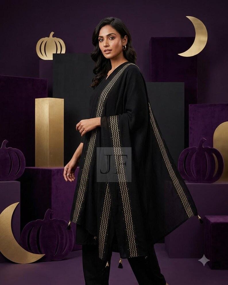 May include: A black tunic and matching trousers paired with a black shawl featuring gold wavy embroidered borders and small black tassels at the corners. The garment is adorned with subtle gold detailing along the edges of the fabric.