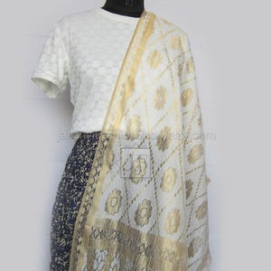 May include: A white and gold patterned scarf draped over a white shirt and a dark blue patterned skirt. The scarf features a floral design and a gold border. The text "Jahanvi Fashion Shop etsy.com" is visible.