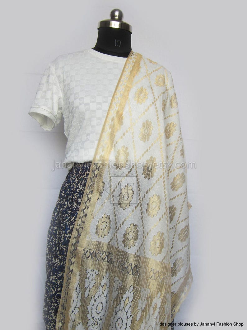 May include: A white and gold patterned scarf draped over a white shirt and a dark blue patterned skirt. The scarf features a floral design and a gold border. The text "Jahanvi Fashion Shop etsy.com" is visible.