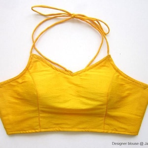 May include: A bright yellow halter top blouse with a criss-cross strap design. The blouse is made of a smooth, silky fabric.