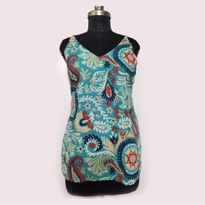 May include: A teal V-neck tank top with a paisley pattern in red, white, and navy blue. The sleeveless top is displayed on a black mannequin. The fabric has a floral design.