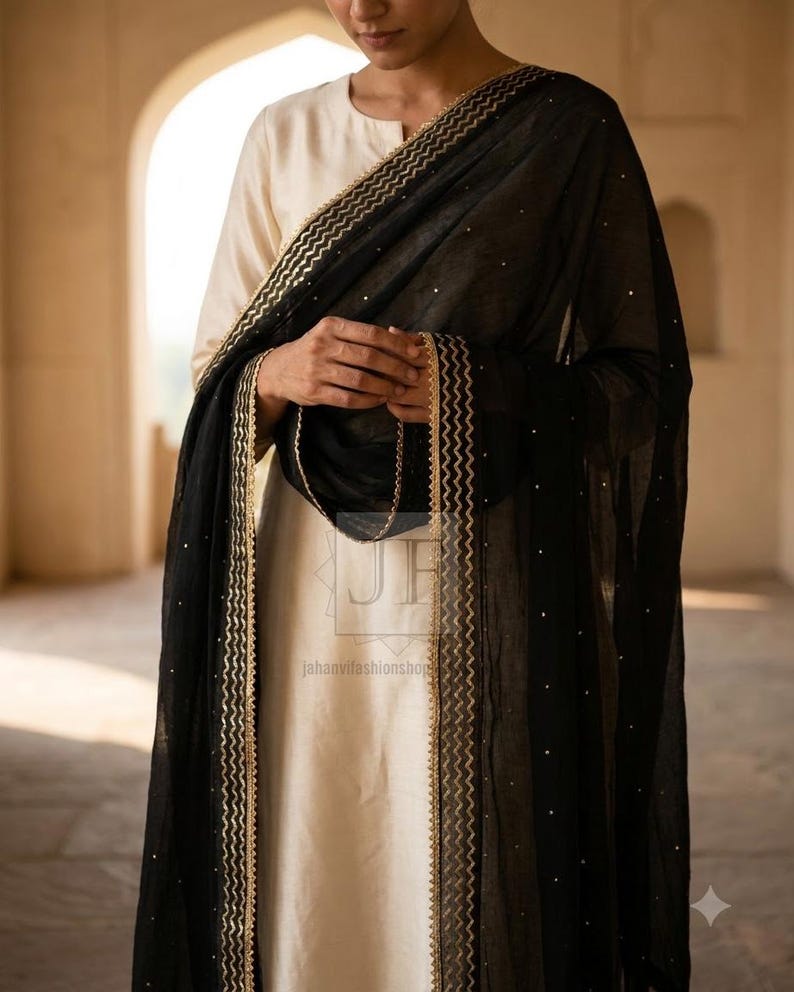 May include: A cream-colored long-sleeved tunic paired with a sheer black dupatta featuring gold zigzag trim along the edges and small scattered gold embellishments. The fabric is lightweight and draped, with the text jahanvifashionshop visible.