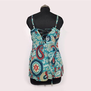 May include: A teal tank top with a paisley pattern in red, blue, and cream. The top features thin straps and a lace-up back detail. The fabric has a floral and paisley design.