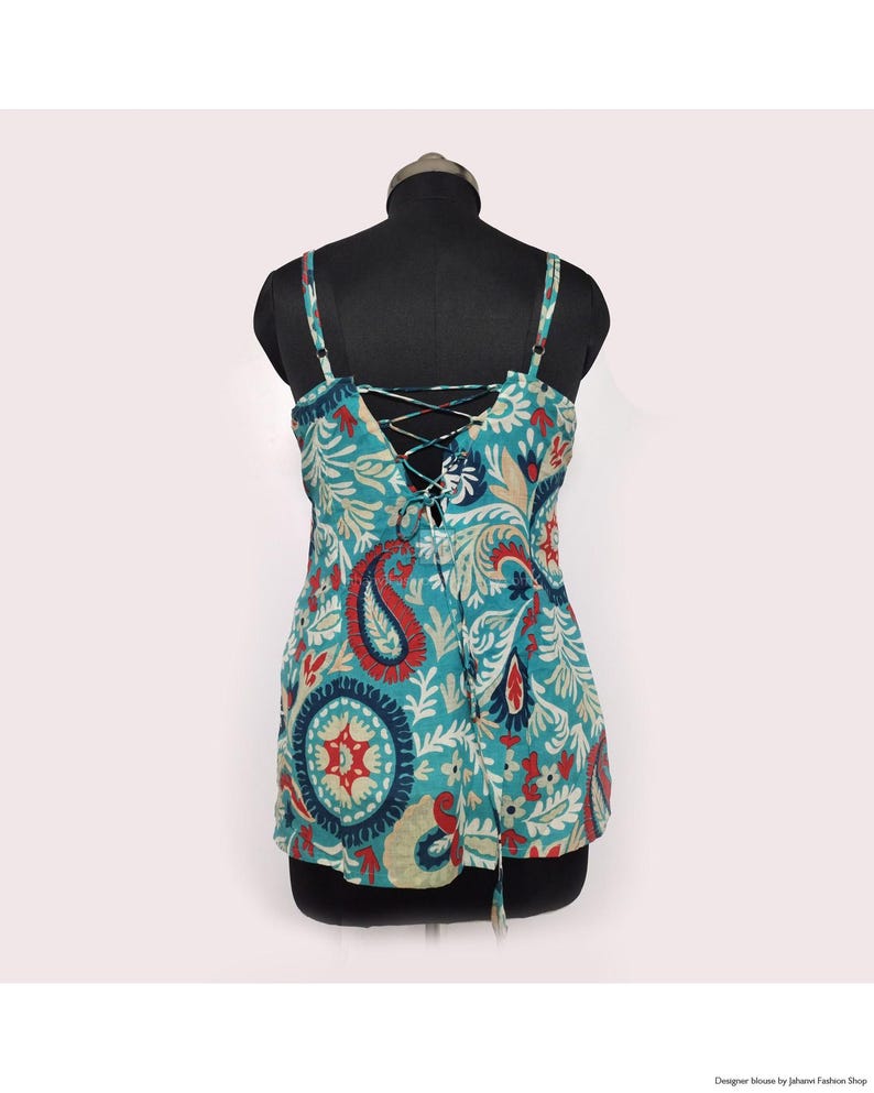 May include: A teal tank top with a paisley pattern in red, blue, and cream. The top features thin straps and a lace-up back detail. The fabric has a floral and paisley design.