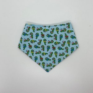 Könnte beinhalten: Ein hellblaues Bandana mit einem weißen Streifenmuster und einem sich wiederholenden Muster von grünen Schildkröten, die rote und gelbe Schwimmreifen tragen und blaue und weiße Strandbälle halten.