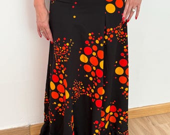 Op de afbeelding: Zwarte maxi-rok met een patroon van oranje en gele cirkels. De rok heeft een gefranjerde zoom en een hoge taille. Het ontwerp doet denken aan een stippenpatroon, wat een opvallende look creëert.