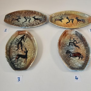 Może przedstawiać: Cztery owalne ceramiczne naczynia z teksturowanymi brązowymi i beżowymi szkliwami. Każde naczynie przedstawia ręcznie malowane czarne postacie myśliwych i zwierząt. Naczynia są ponumerowane od 1 do 4 za pomocą małych białych etykiet pod spodem.