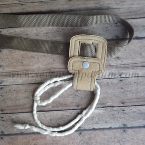 May include: A tan felt belt loop with a metal button and a white cord attached. The loop is designed to hold a belt.