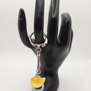 May include: A silver keychain with a blue and yellow miniature cowboy hat charm.