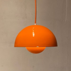 Op de afbeelding: Een feloranje hanglamp met een koepelvormige kap. De lamp hangt aan een dun koord.