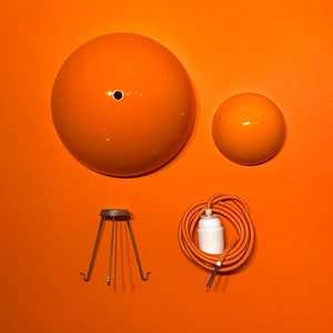 Könnte beinhalten: Ein Satz orangefarbener Lampenschirme, ein Lampenschirmhalter aus Metall und ein Kabel mit einer Lampenfassung. Die Lampenschirme sind rund und haben eine glatte, glänzende Oberfläche.
