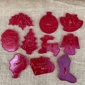 May include: A set of ten red translucent plastic cookie cutters in various holiday shapes including a holly leaf, a round ornament, a bell, a Santa face, a Christmas tree, a reindeer, an angel, a wreath, a gift box with Merry Christmas text, and a stocking.