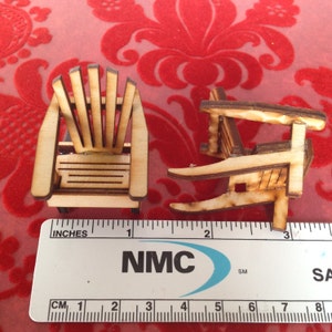 May include: Two miniature wooden chairs, one with a slatted back and the other with a solid back, are shown next to a ruler marked in inches and centimeters. The chairs are approximately 1 inch tall.
