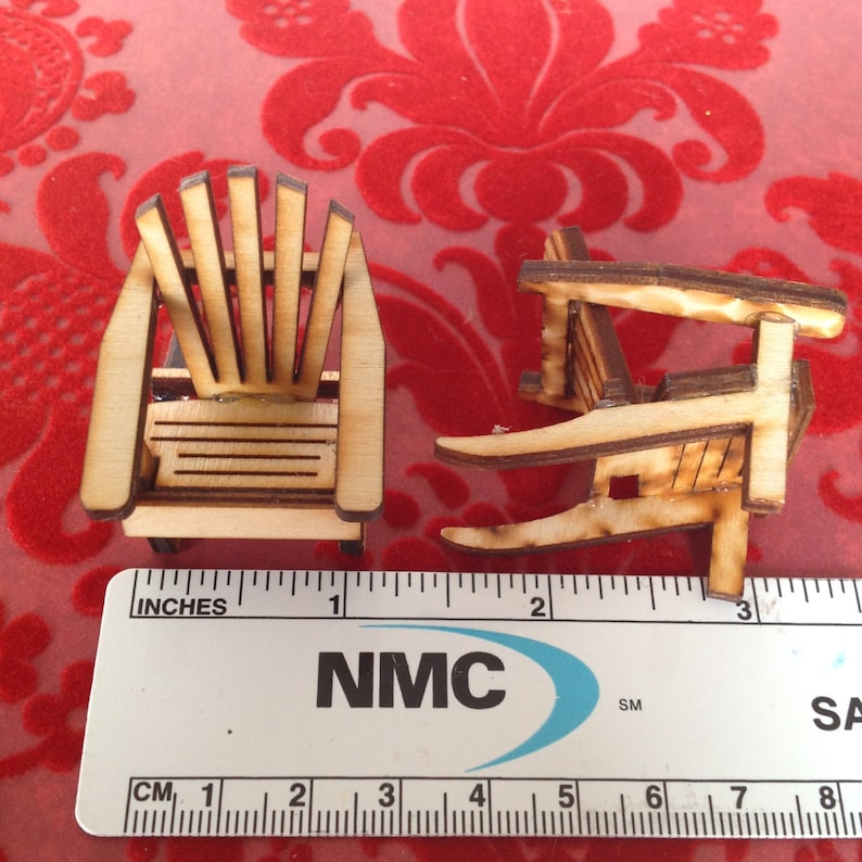 May include: Two miniature wooden chairs, one with a slatted back and the other with a solid back, are shown next to a ruler marked in inches and centimeters. The chairs are approximately 1 inch tall.