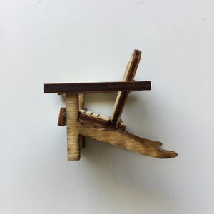 May include: A miniature wooden adirondack chair with a brown stained seat and back. The chair is made of light wood and has a simple design.