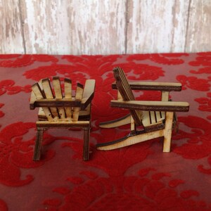 May include: Two miniature wooden chairs in a classic adirondack style, with a natural wood finish. The chairs are sitting on a red velvet surface.