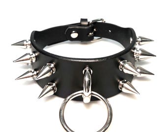 Puede incluir: Una gargantilla de cuero negro con dos filas de púas de metal plateado y una gran junta tórica central plateada. El collar incluye un cierre de hebilla ajustable con un pasador de metal y una serie de orificios para ajustar el tamaño.