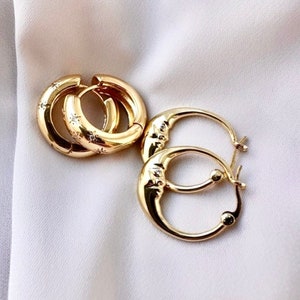 Peut inclure: Deux paires de boucles d'oreilles créoles en or. Une paire a une finition lisse, tandis que l'autre paire a une finition texturée avec de petites étoiles.